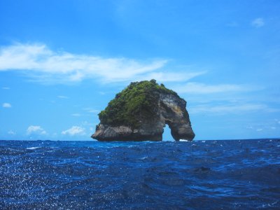 arched rock island under blue and white cloudy sky