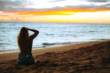 woman sitting on seashore looking at sea during golden hour photo