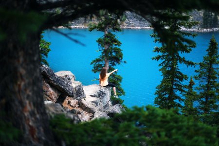 girl sitting on cliff near trees pointing towards body of water photo