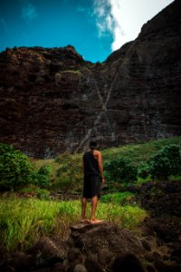 man wearing white black tank top and shorts standing on rock photo