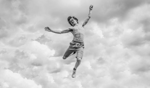 grayscale photo of person jumping overlooking clouds photo