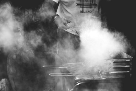 grayscale photo of man standing near gas grill photo