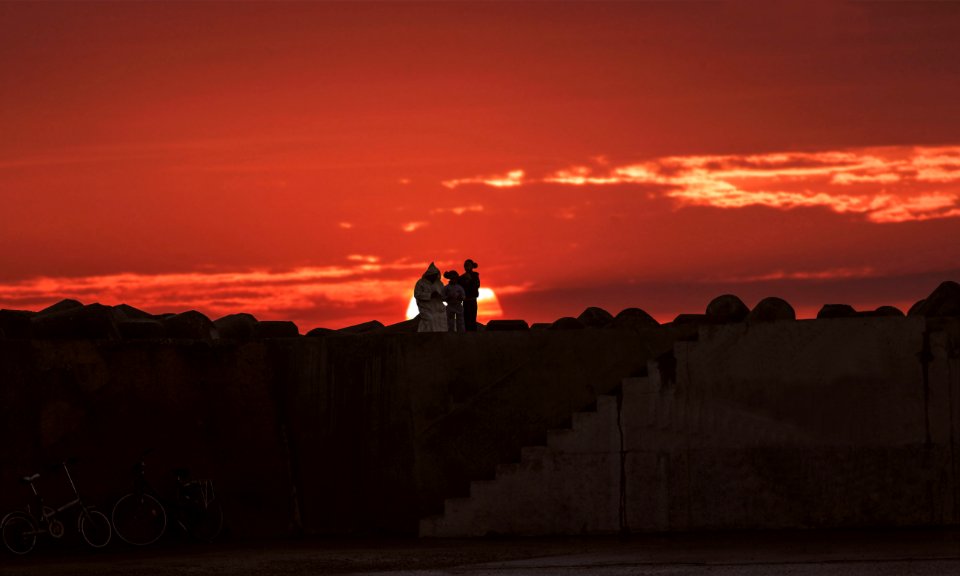 silhouette of man and woman sitting on concrete wall during sunset