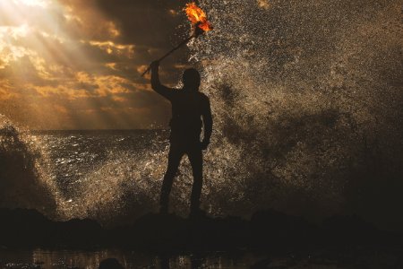 A man standing in the water during sunset at dusk, while holding a torch. photo