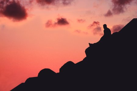 silhouette of man sitting on cliff photo