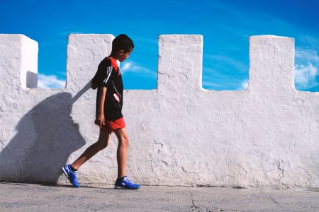 boy walking beside white concrete wall photo