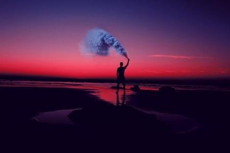 silhouette of man standing on seashore holding smoke can photo