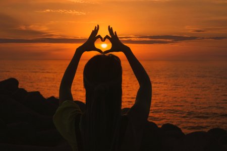 silhouette of woman doing heart sign during sunset photo