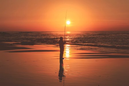 silhouette photography of person holding fishing rod near body of water photo