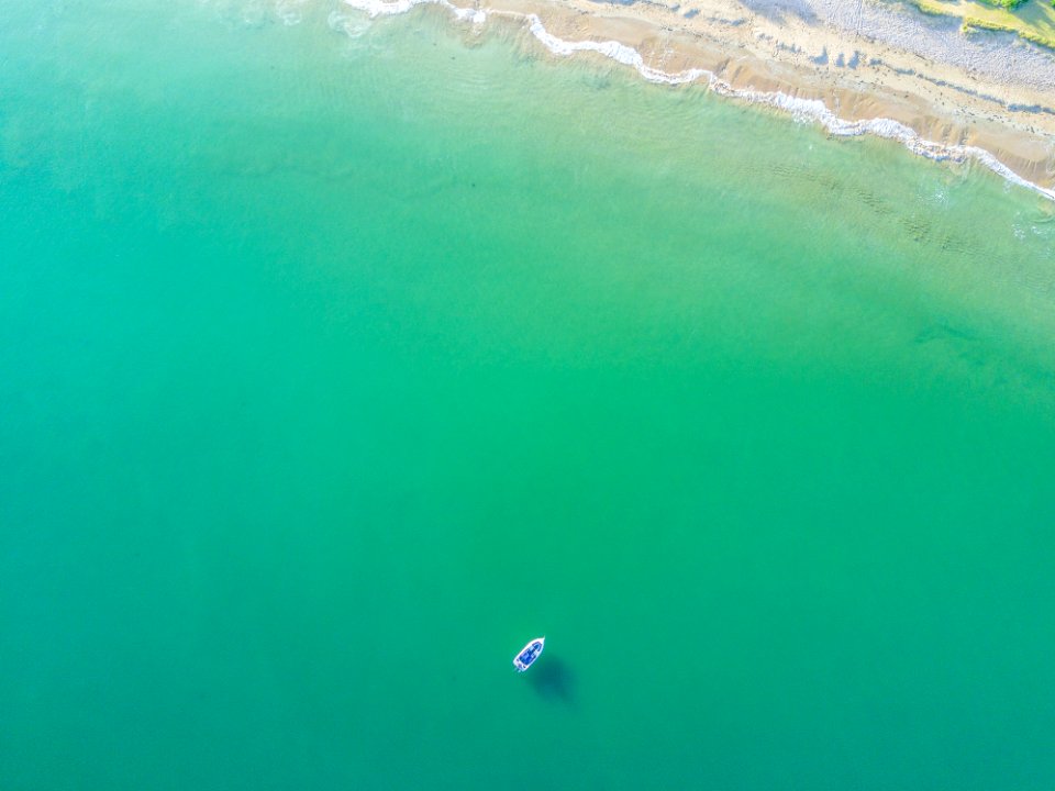 aerial photography of white boat on green ocean near seashore