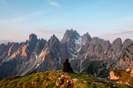 man sitting on cliff facing gray mountain photo