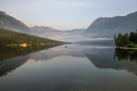 body of water near mountain ranges with green vegetation covered with fog during daytime photo