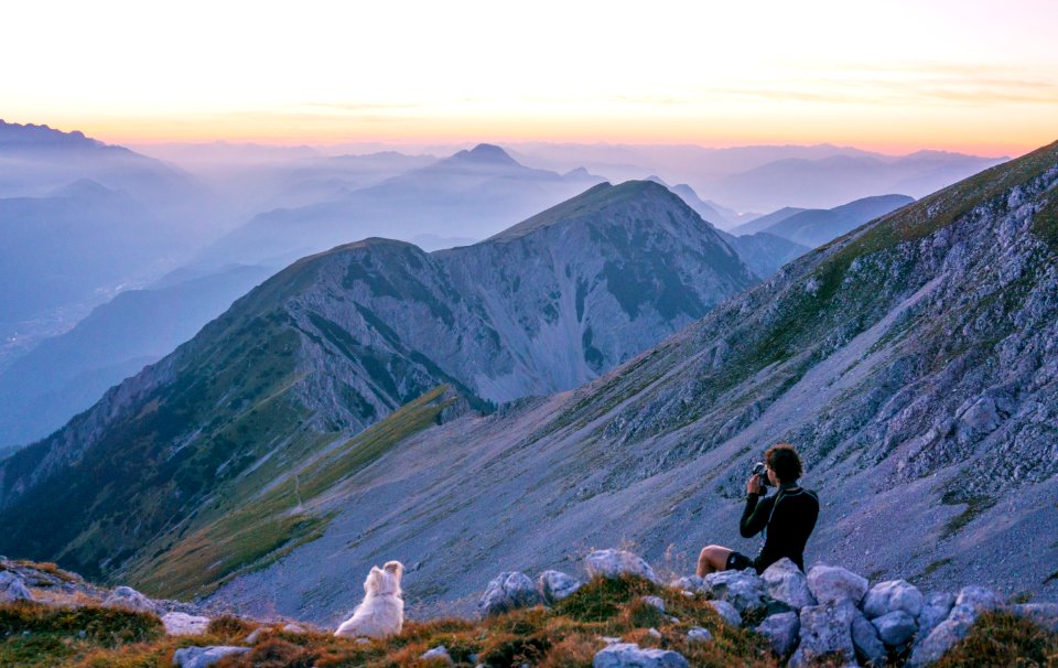 person sitting on mountain near white dog during daytime