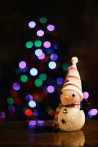 A little snowman figure sitting on the floor in front of a Christmas tree. photo