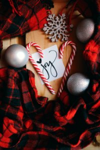 A white note that says "Joy," surrounded by candy canes, XMAS ornaments and red plaid material. photo