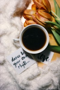 A black cup of coffee in a small cup, surrounded by flowers. photo