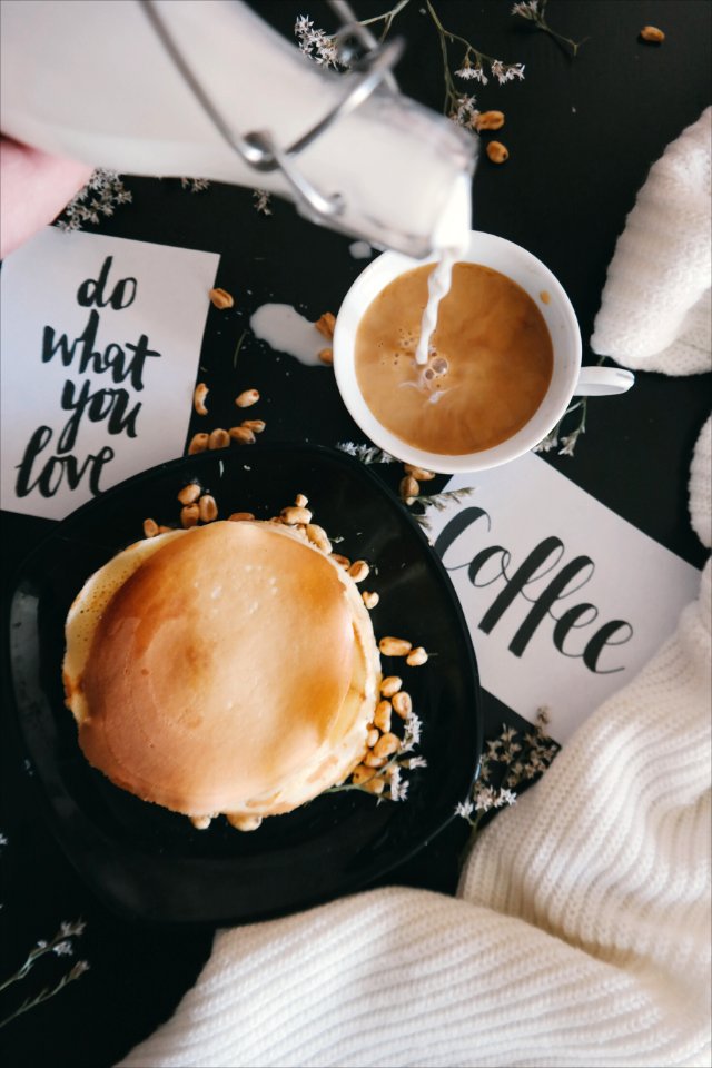 A plate of food with a cup of coffee, taken while someone pours sugar into the drink. photo