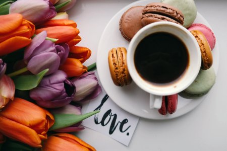A black coffee in a small cup on top of a plate, surrounded by flowers and snacks. photo