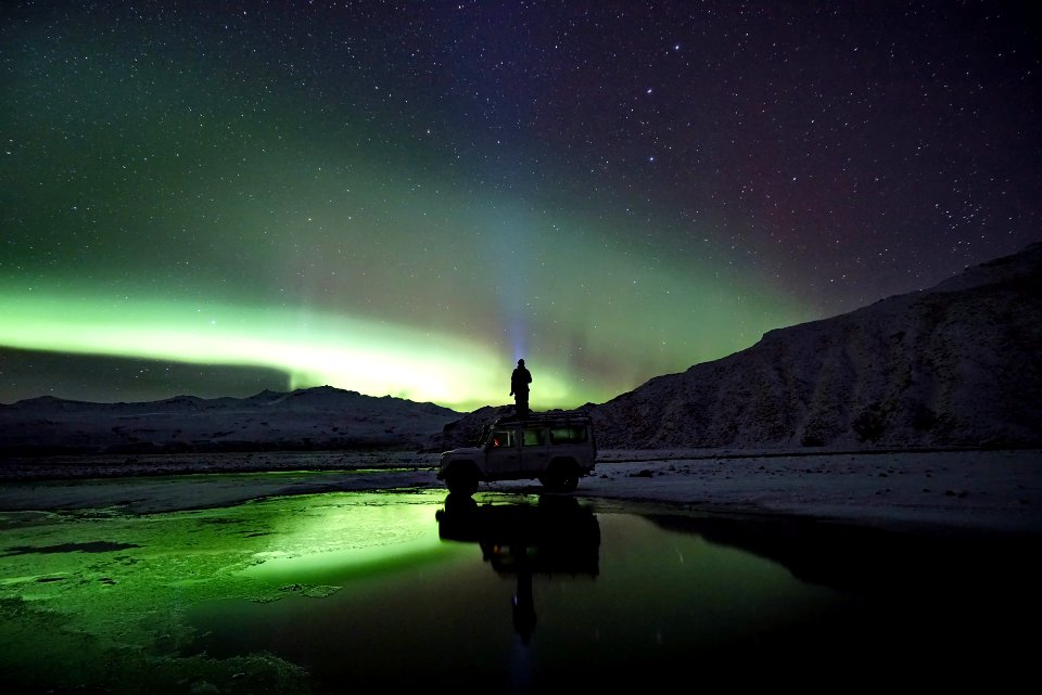 man standing on SUV watching northern lights