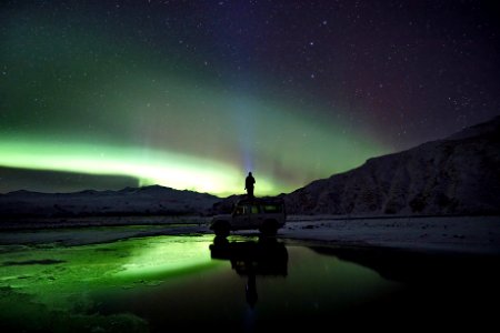 man standing on SUV watching northern lights photo