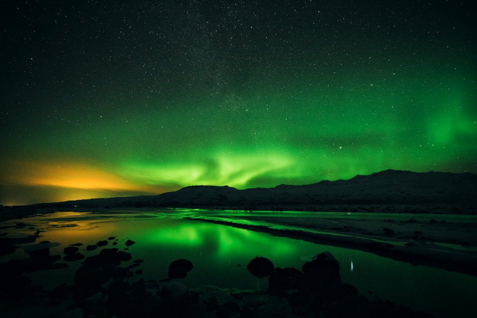 calm of water near mountain under aurora borealis at night time