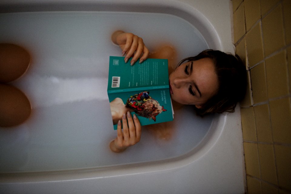 woman lying on bathtub with green book