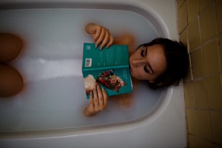 woman lying on bathtub with green book photo