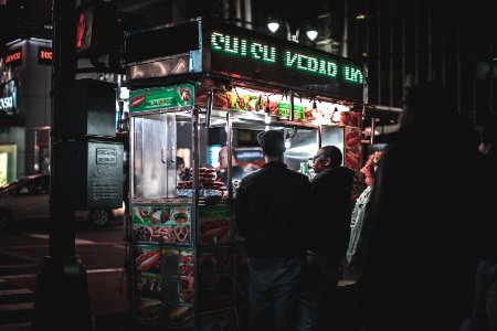 two men standing in front of food cart besides black post during nighttime photo