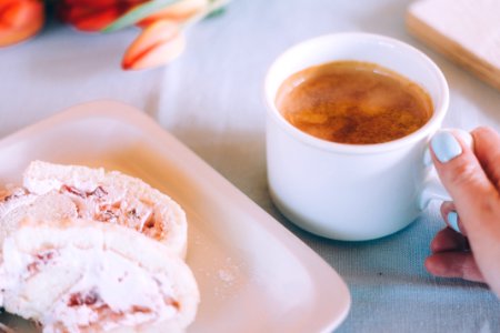 white mug filled with brown liquid beside tray with pastry photo