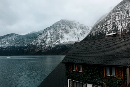 black and brown painted 2-story house near body of water and gray mountains covered with snow during daytime photo