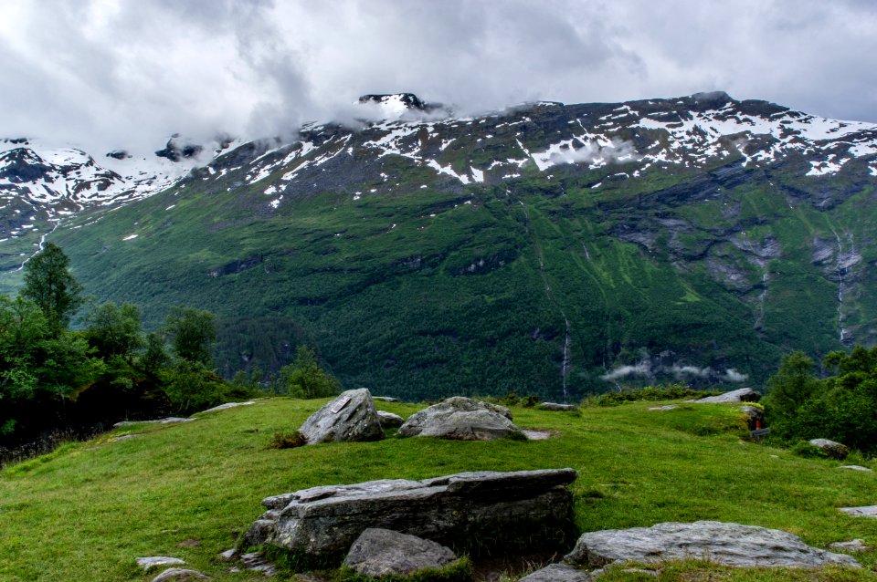 gray and black rocks surrounded by green grass near mountain under white sky at daytime
