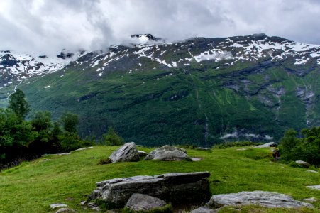gray and black rocks surrounded by green grass near mountain under white sky at daytime photo