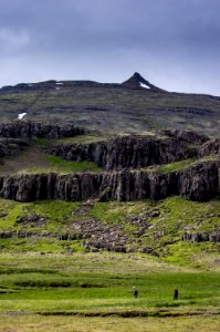 two person walking on green grass field with mountain photo