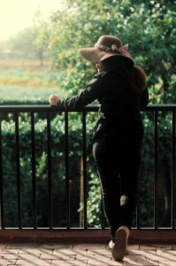 woman in black jacket and black pants wearing brown hat standing beside black metal fence during