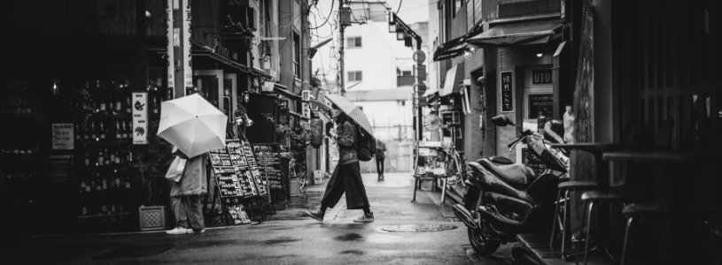 grayscale photo of man in black coat walking on street photo