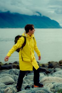 boy in yellow jacket standing on rock near body of water during daytime