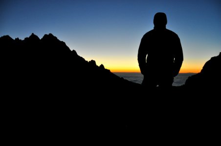 silhouette of person on top of mountain under blue sky during orange sunset photo