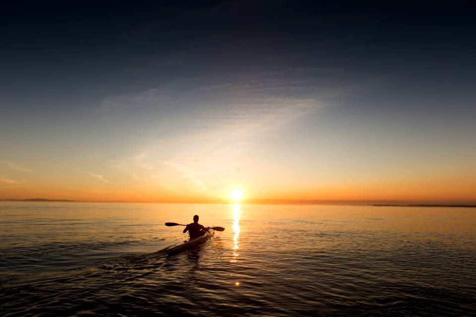 man riding kayak on water taken at sunset