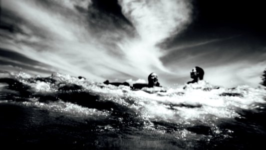 grayscale photo of two persons swimming on body of water photo