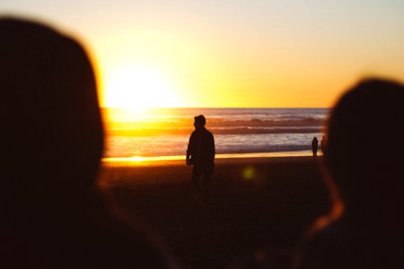 silhouette photo of man standing near seashore at sunset photo