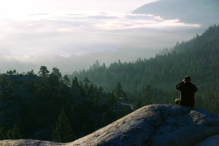 man sits on the mountain facing landscape view