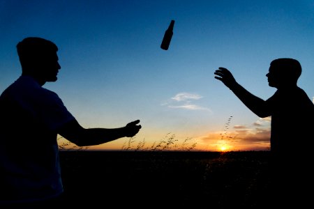 silhouette photo of two men throwing bottle during daytime photo