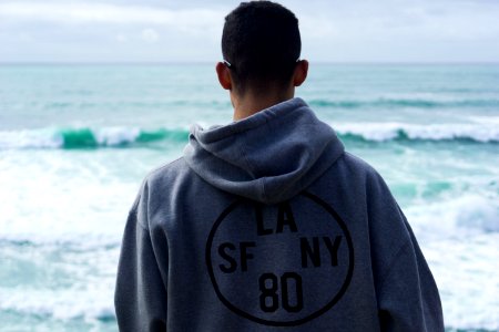 man wearing grey pullover hoodie standing on shore overlooking body of water during daytime photo