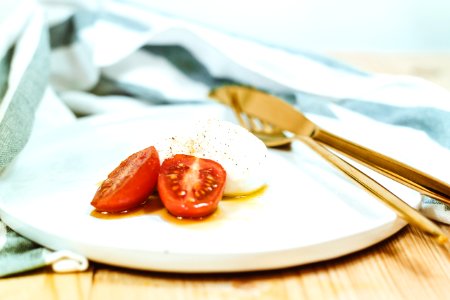 sliced tomato and mozzarella cheese on white plate beside brass-colored knife and fork photo