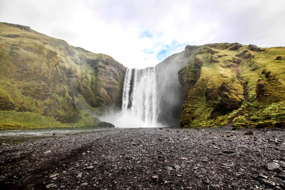 photo of waterfall near mountain under blue sky at daytime