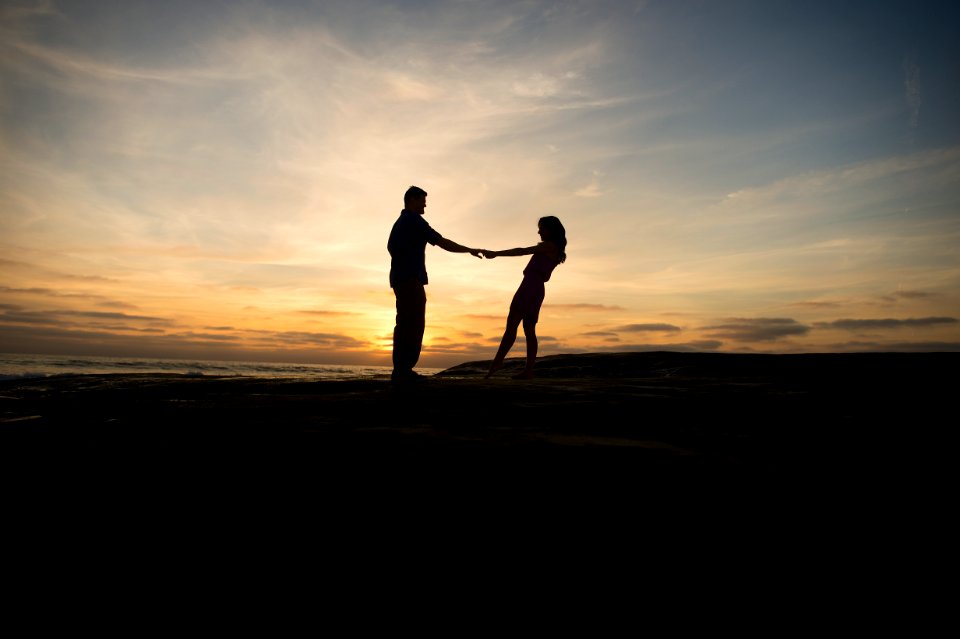 Couple spins round holding hands, silhouetted against setting the sun