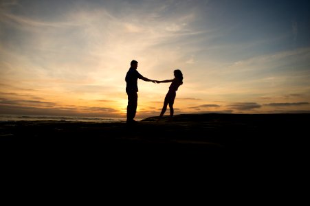 Couple spins round holding hands, silhouetted against setting the sun photo