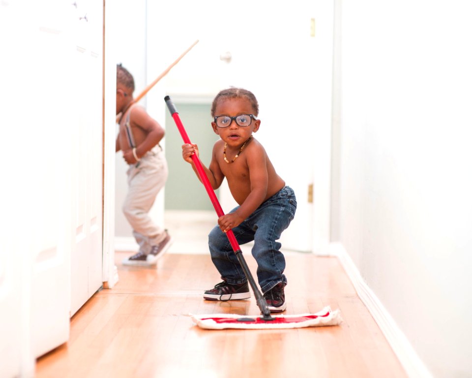 A funny African American Boy with glasses, using a push mop to clean the haul away.