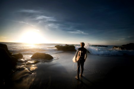 man standing carrying surfboard near seashore during daytime photo