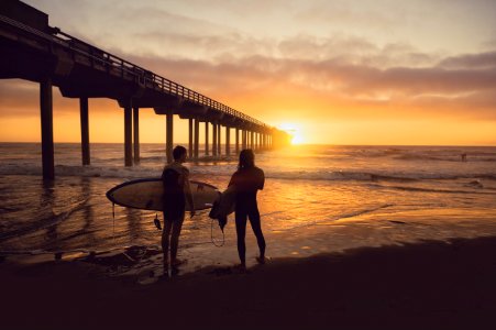 woman carrying surfboard beside person during sunset photo